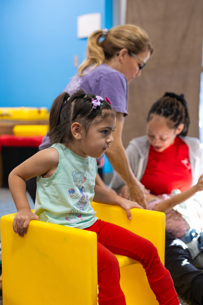 young girl sitting in a yellow preschool cube chair using her hands to push her body upright