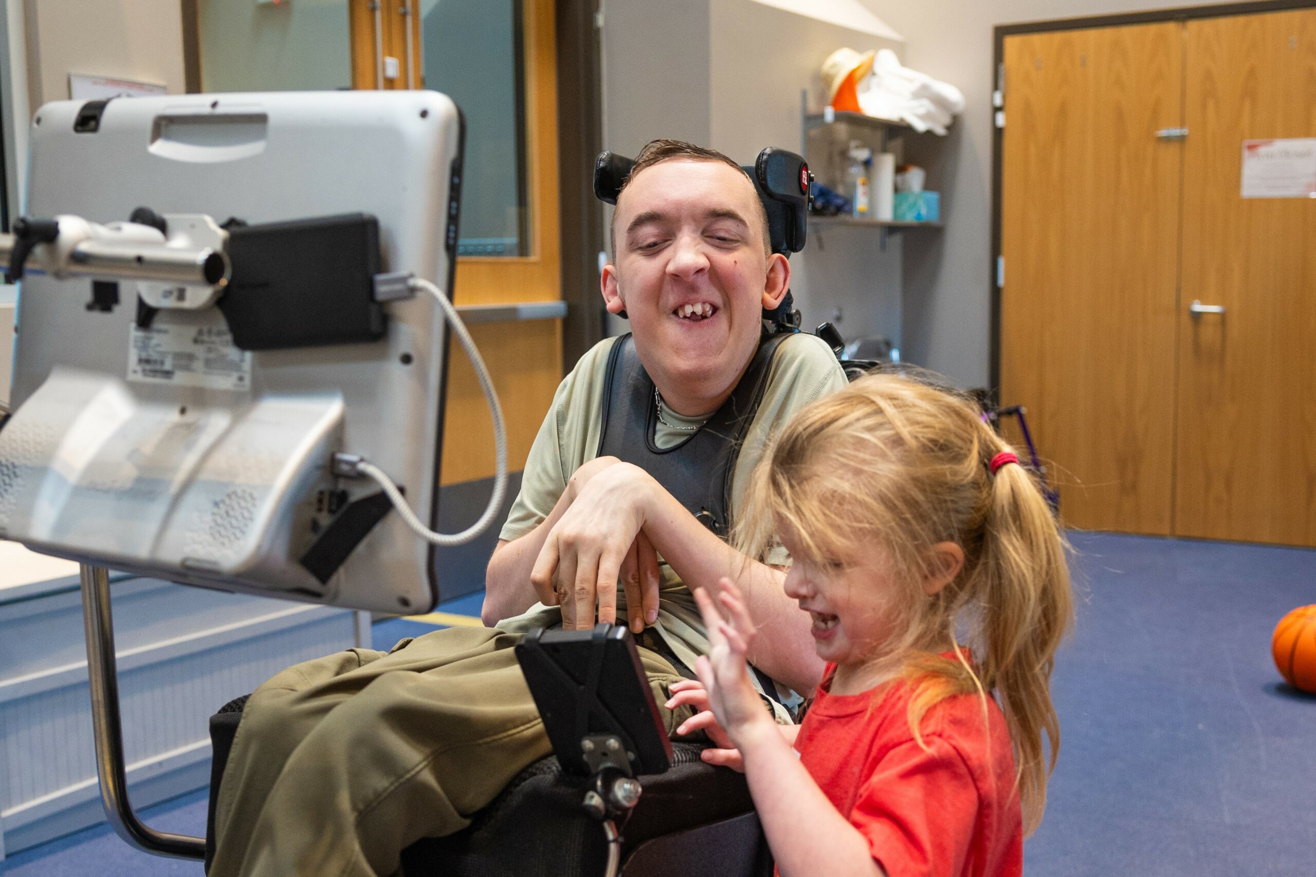 Young man with Cerebral Palsy using a voice output device to communicate with a young student.